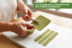 A person using gold-handled scissors to cut an olive green adhesive strip to size on a white cutting board, with three additional strips and a green text overlay that reads 'CUT TO SIZE FOR A CUSTOM FIT ON ANY FINGER OR KNUCKLE'.